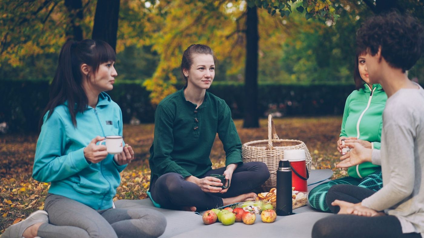 Friends sitting together outdoors with mugs of tea on an autumn day