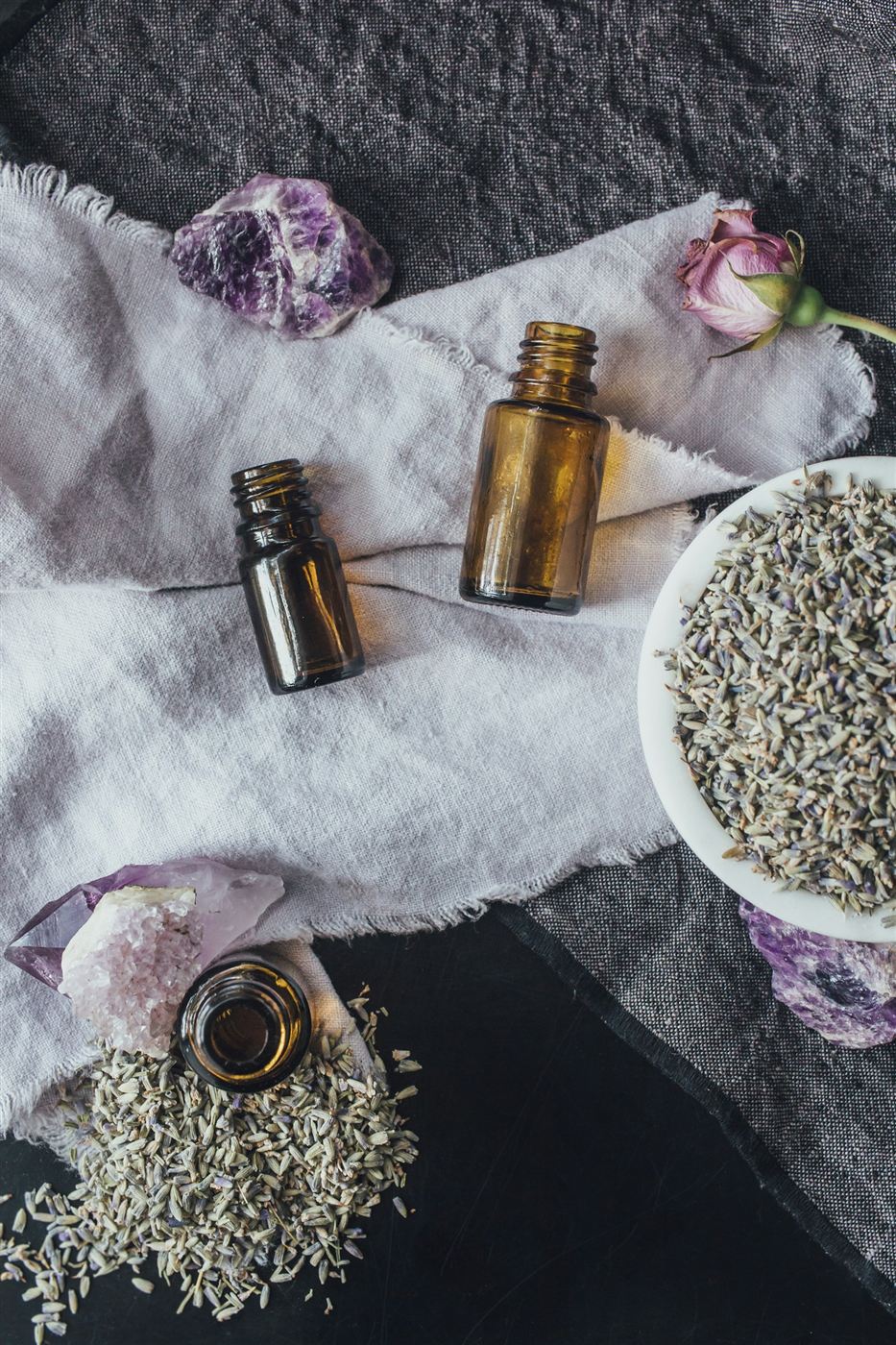 Small amber bottles of lavender oil beside a bowl of dried lavender
