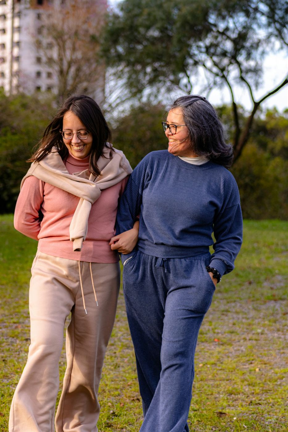 Two women walking arm in arm through a park, laughing together